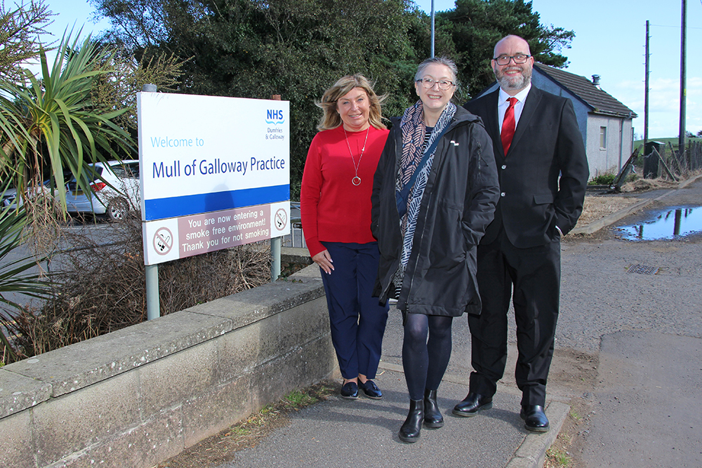 Image shows three people, standing beside a sign for the Mull of Galloway Practice.